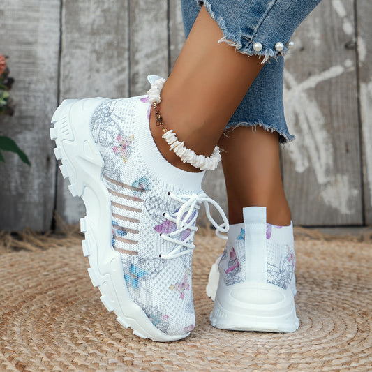 White sneakers with floral patterns worn by a person on a textured surface.