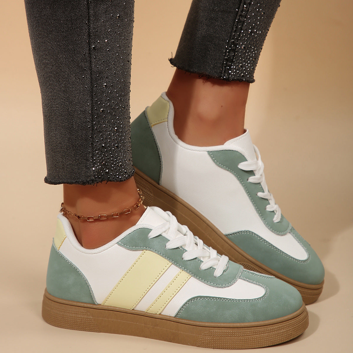 Colorful sneakers with white, green, and yellow accents worn with dark jeans on a beige background.