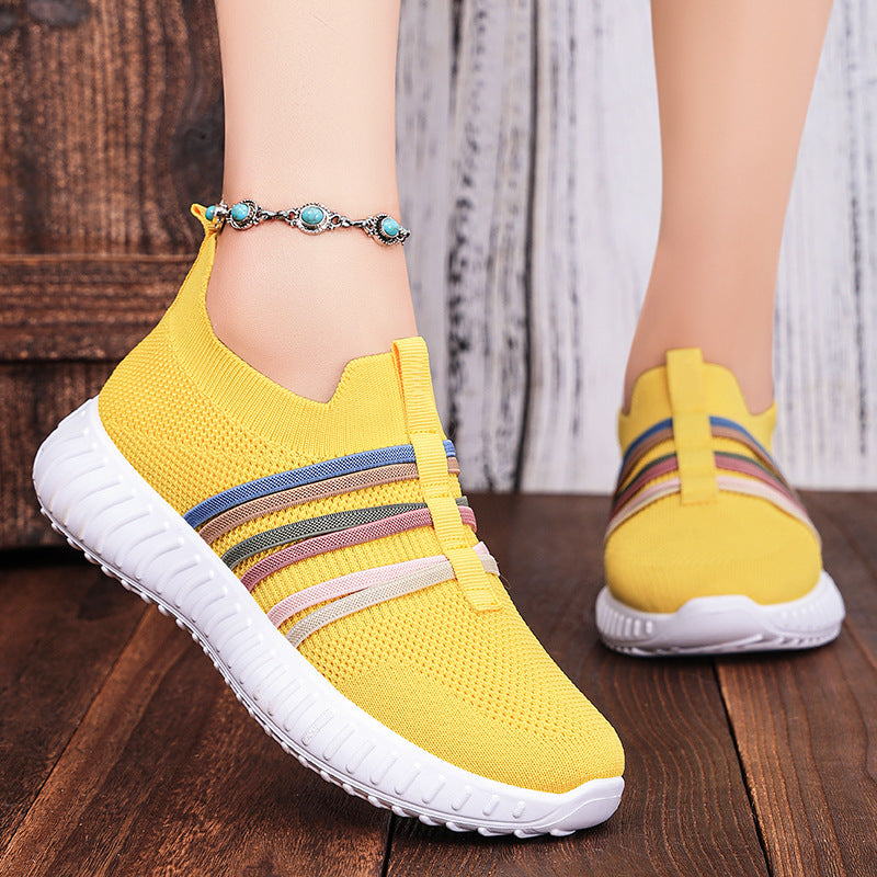 Yellow sneakers with colorful stripes worn on a wooden floor.
