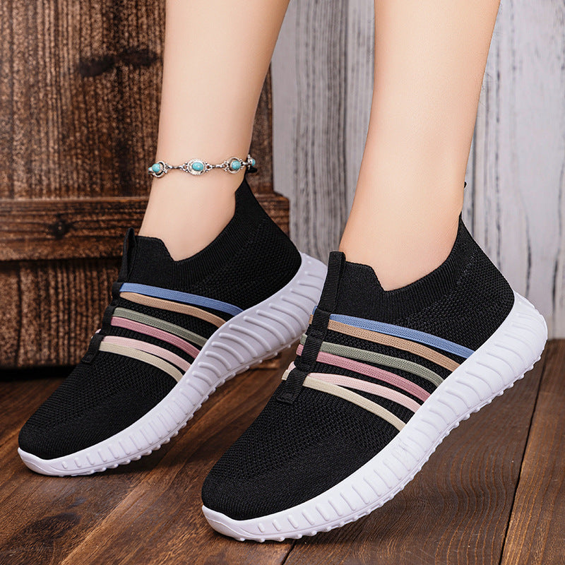 Black slip-on sneakers with colorful stripes on a wooden floor