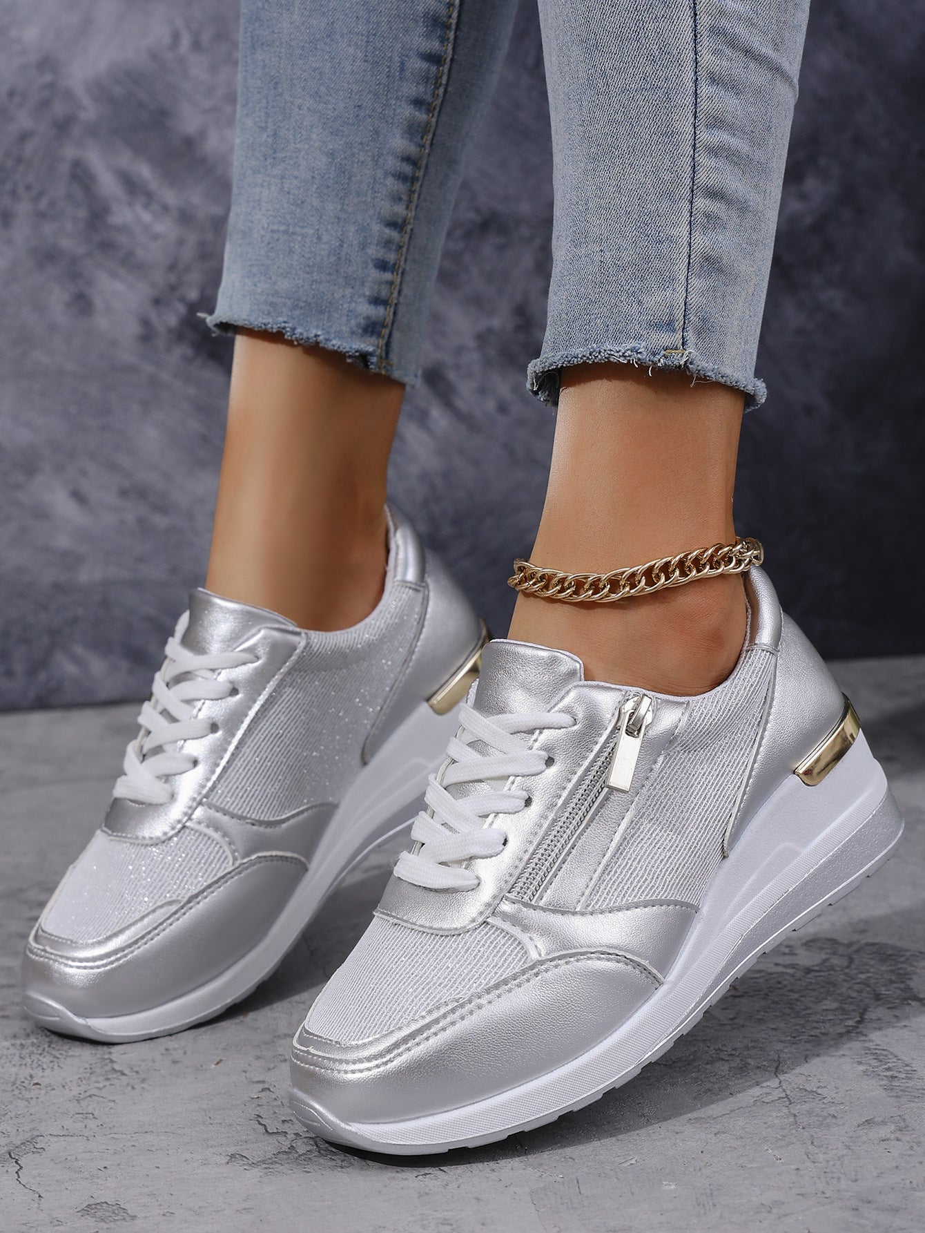 Silver sneakers worn with light blue jeans on a gray surface.