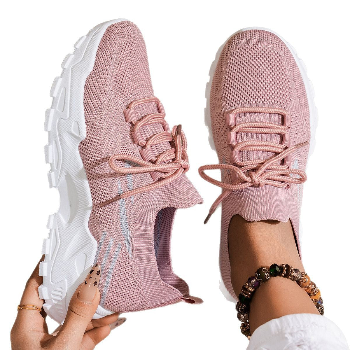 Pink sneakers with white soles held by a person on a white background