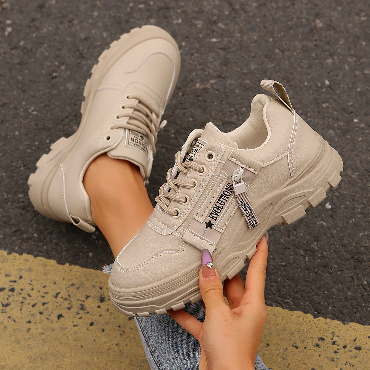 Beige sneakers with visible branding held by a hand on a pavement background