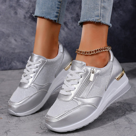 Silver sneakers worn with light blue jeans on a gray surface.