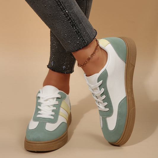 Pair of green and white sneakers with brown soles worn by a person on a beige background