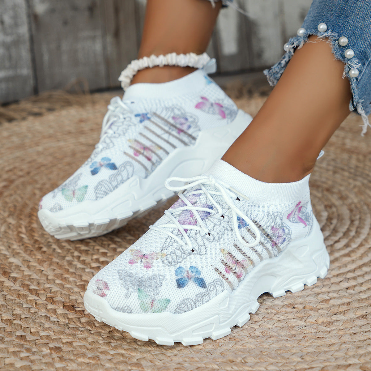 White sneakers with butterfly patterns worn by a person on a woven surface